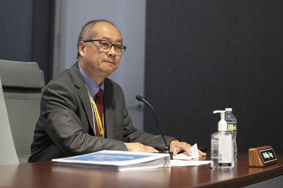 A man in a suit sits in front of a podium, looking up at an off-camera grou pof people