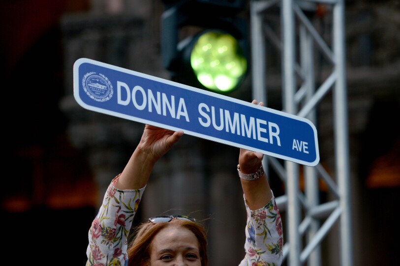 A woman holds up a sign that reads "Donna Summer Avenue".