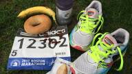 Sneakers, a marathon bib, and snacks laid out on the grass at Athlete's Village.