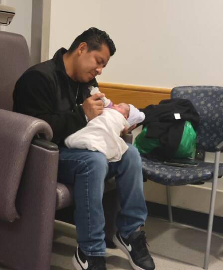 A man is sitting with a newborn in his lap and holding a baby bottle.