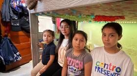 A young adult and three girls sit in a children's bedroom. Their faces are stoic.