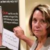 A white woman looks at the camera as she puts her hand next to a poster with a photo of a young white man and the words "Sex trafficking kills"