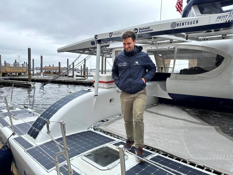 A man stands on the platform of a boat docked in a harbor.