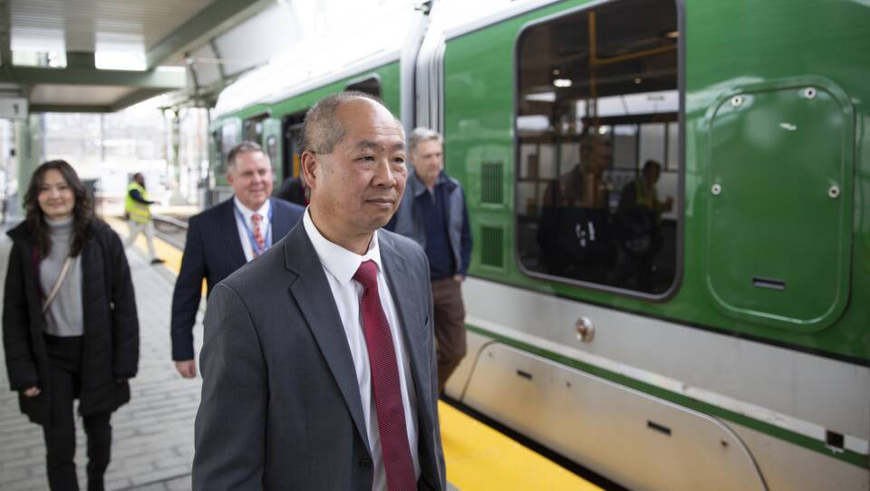 A man in a suit and tie walks down an MBTA platform.
