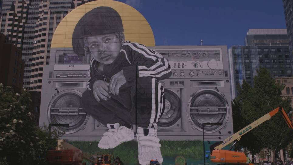 A mural of a young boy squatting and looking out at the viewer in front of a boom box