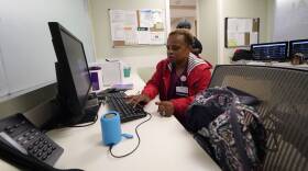 A woman types one-handed on a computer keyboard while working in a hospital.