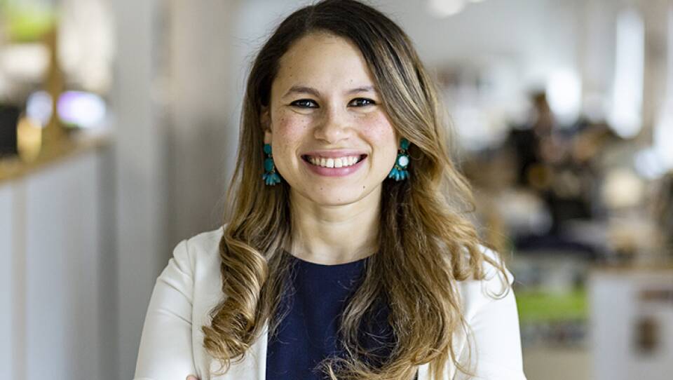 A woman in a white jacket, dark blue shirt, and dangling turquoise earrings smiles at the camera.