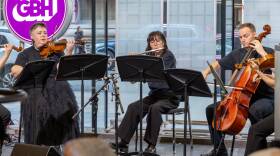 Three musicians seated in a studio perform on the violin, flute and cello.
