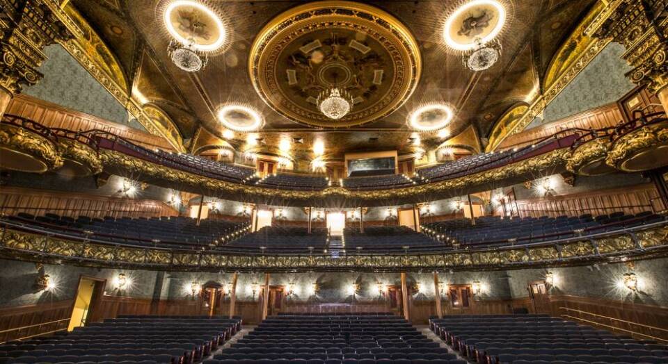 Inside a large, grand theater, looking up into the empty seats and mezzanine.