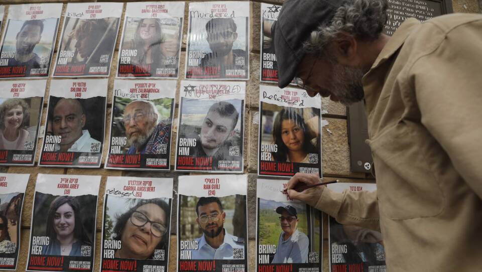 A man uses a pen to write on a hostage poster affixed to a wall.