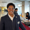 A man poses for a picture in front of a conference registration table in the corridor of  an academic building