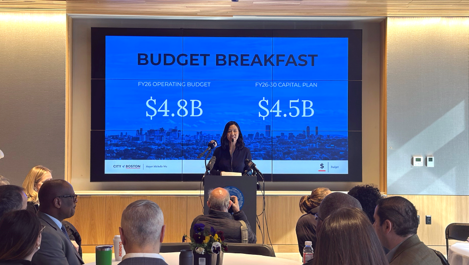 Wu addresses a room in front of a slide that reads "Budget Breakfast".