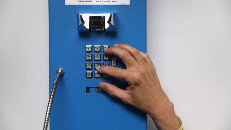 A woman's hand dials a blue wall phone.
