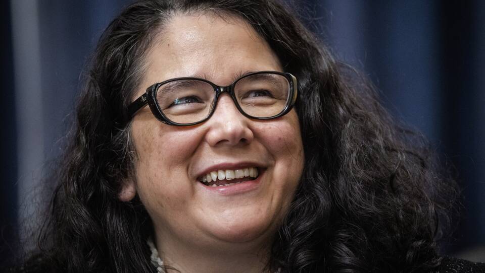 A close-up of a woman with dark-rimmed glasses, smiling.