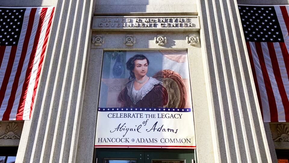 A banner of Abigail Adams hangs between two American flags on a Quincy building