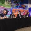 Five men and one woman, all wearing suits, speak during a political debate as they sit along one edge of a long table.