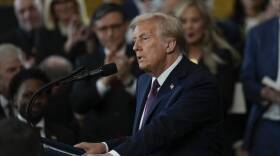 Donald Trump stands at a lectern and speaks in front of a crowded room of people.