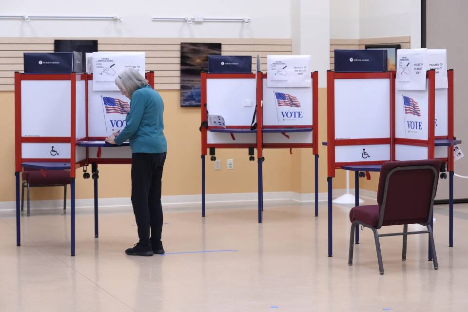 A person stands at a polling booth set up in a large room.