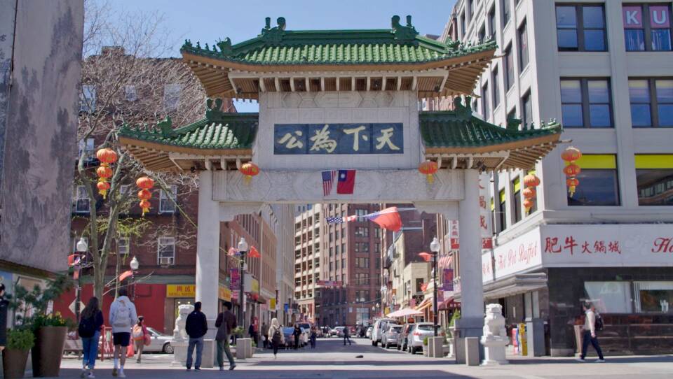 A large arch with Chinese writing sits in front of a number of city buildings.