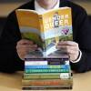 A person holds open the book "Gender Queer" to read while resting it atop other challenged books, including "The Bluest Eye" and "Lolita"