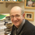 Old White Man in front of a book shelve and family photos