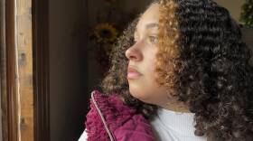 A young woman looks out a window, with the sunlight shining on her face.