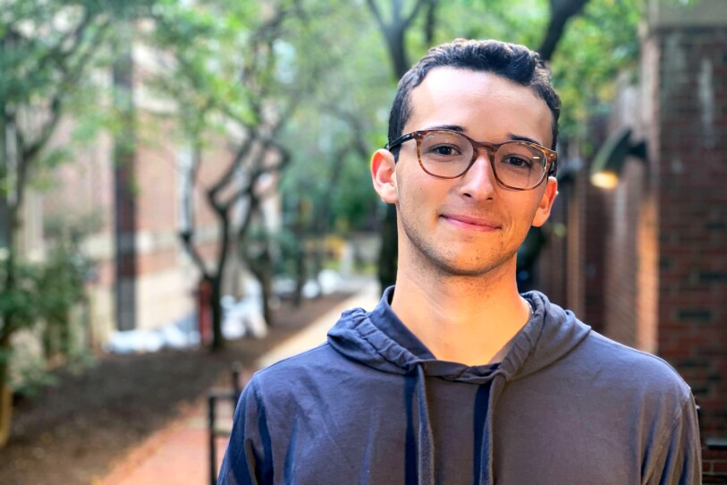 A young man wears a drawstring hoodie and horn-rimmed glasses on Harvard's campus