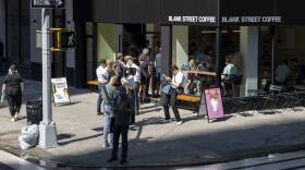 Dozens of people wait in line outside of a cafe.