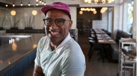 Williams sits in an empty restaurant, smiling at the camera.
