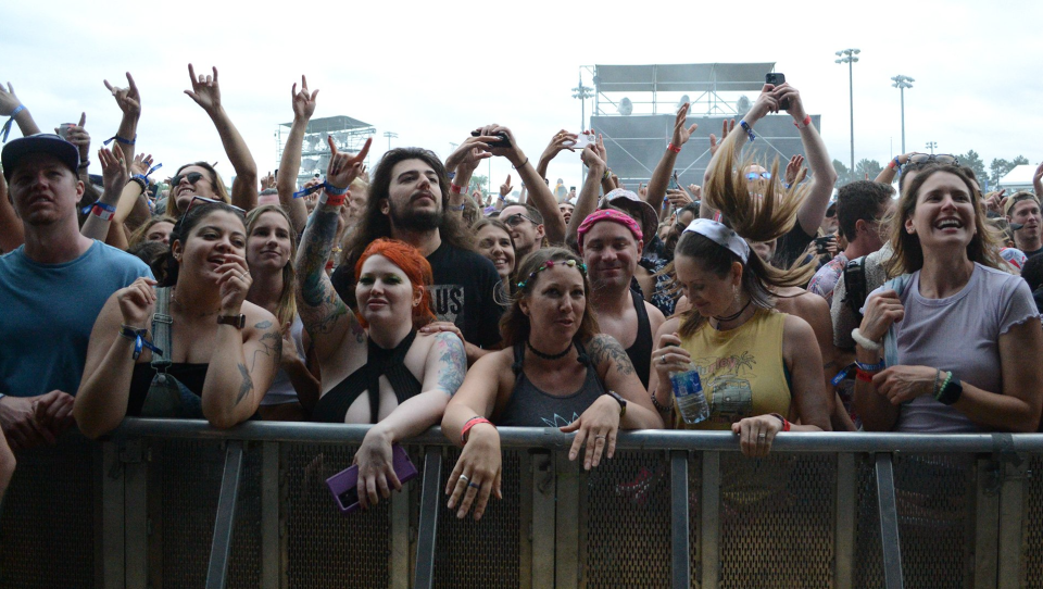 Hundreds of people behind a concert barricade smile, sing and hold up their hands as they watch a show.
