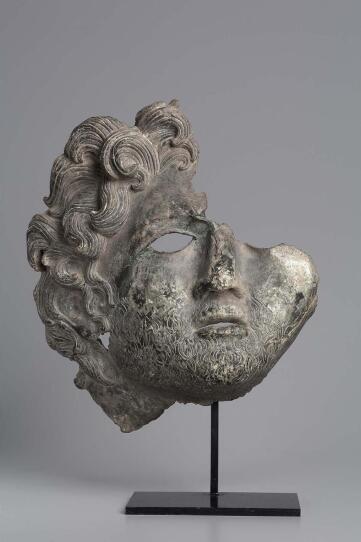 A sorrowful face features curly carvings, emulating a light beard and luscious hair. It's a damaged piece, with one eye and half the scalp missing.