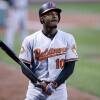A baseball player in a Baltimore Orioles jersey stands in a field, holding a bat.