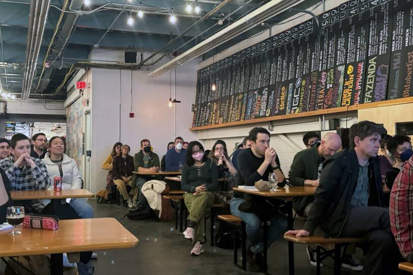 People sit at rows of table in a brewery.