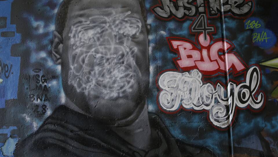 Squiggles of white spray paint cover the face and name of a mural depicting George Floyd, a Black man who was killed by police.