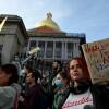 A large crowd of people gathers in front of the Massachusetts State House holding signs in support of reproductive rights.