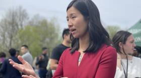 Boston Mayor Michelle Wu looks towards an out-of-frame subject as she responds to a question. She is wearing a red sheath dress.