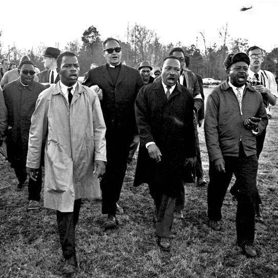 a black and white photograph of John Lewis, Dr. Martin Luther King, Jr., & Ralph Abernathy singing “We
Shall Overcome” on the James Meredith March Against Fear,
Mississippi, June 1966