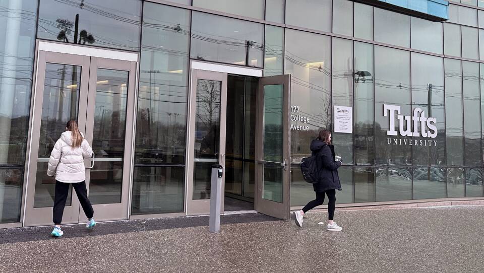 One person enters the door of a large glass building as another person walks out.