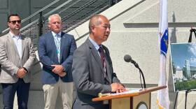 Phil Eng speaks from behind a lectern with the MBTA logo. Two men stand behind him.