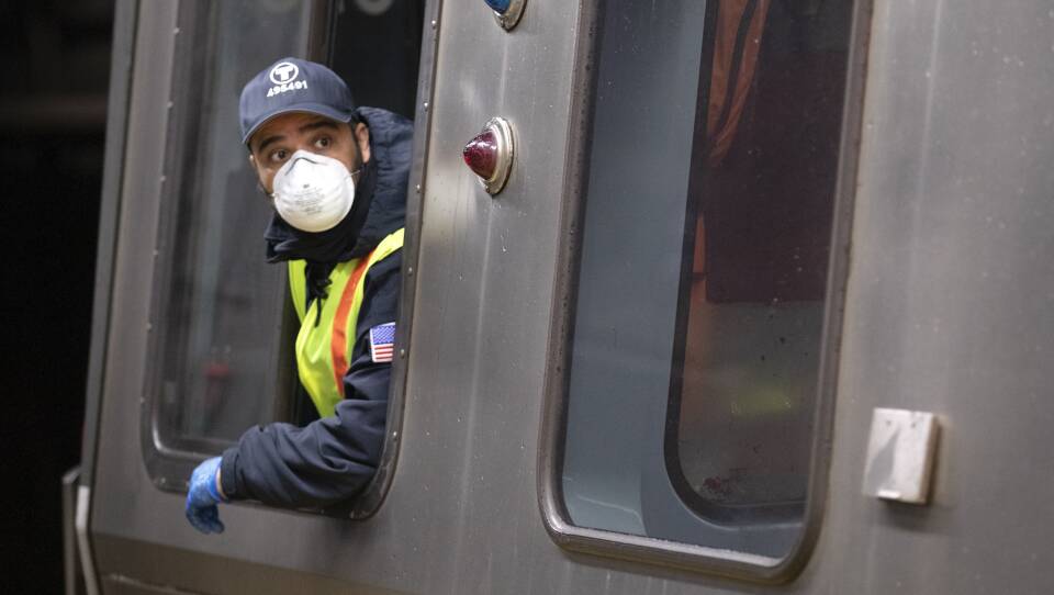 An operator looks off camera, peering out the train while wearing a mask