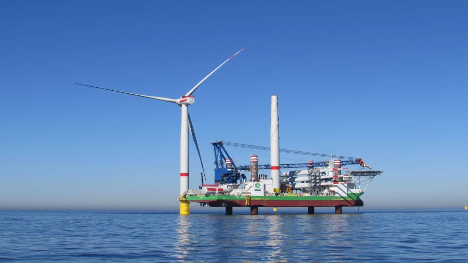 A boat sits just above the water, perched atop four pillars, next to a large wind turbine.