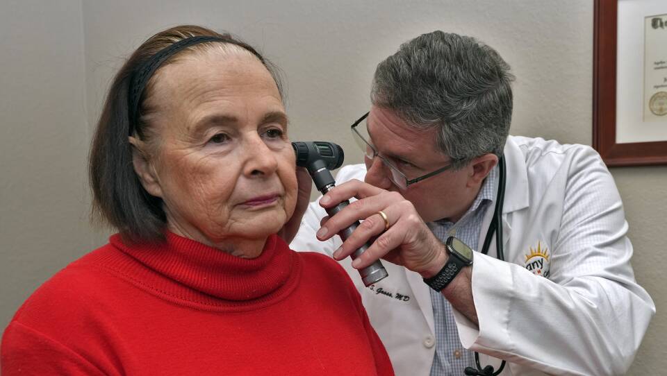 A doctor uses a scope to look in a patient's ear as she looks straight ahead.