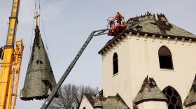 A man in a cherry picker surveys a church, the steeple of which was removed by a crane.