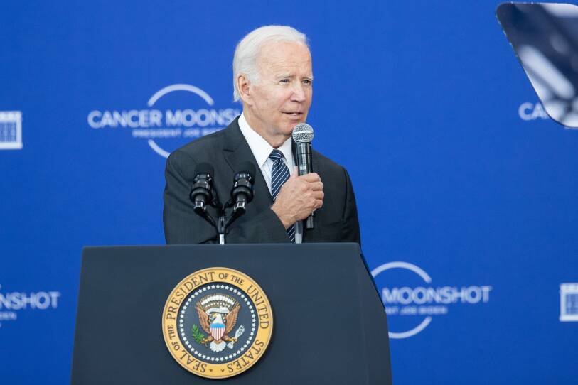 The president speaks from a podium, wearing a suit with "CANCER MOONSHOT" written on the backdrop behind him