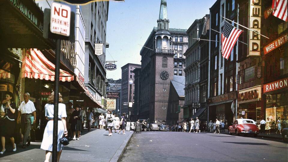 And old colored photograph looking down a busy city street with the Old South Meeting House at the end. Brick church with clock and bell tower.