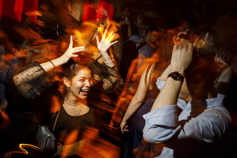 A women dances and smiles in a crowded nightclub surrounded by people.