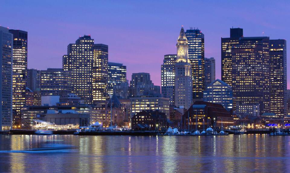 A purple and pink sky lingers over downtown Boston as lights in buildings turn on for the night.