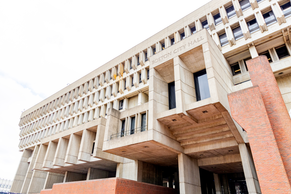 A large brutalist-architecture building with the words "Boston City Hall" over the doorway windows.