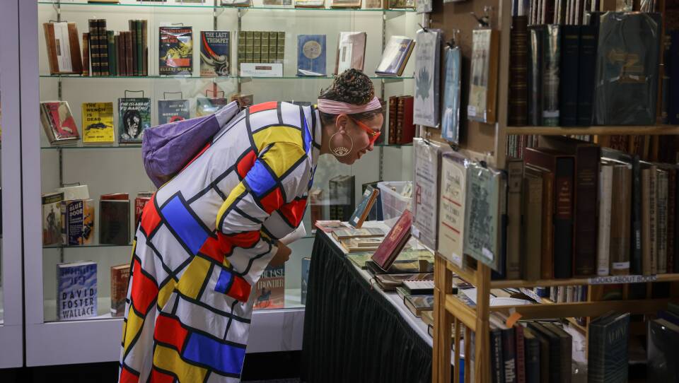 A person wearing a dress in the style of Piet Mondrian's painting "Composition with Red, Blue and Yellow" leans over as they look at a table of books in a store.