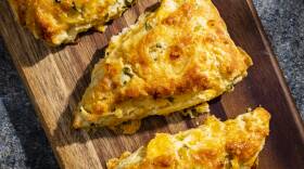 Triangular scones topped with golden brown melted cheese on a long wooden plank
